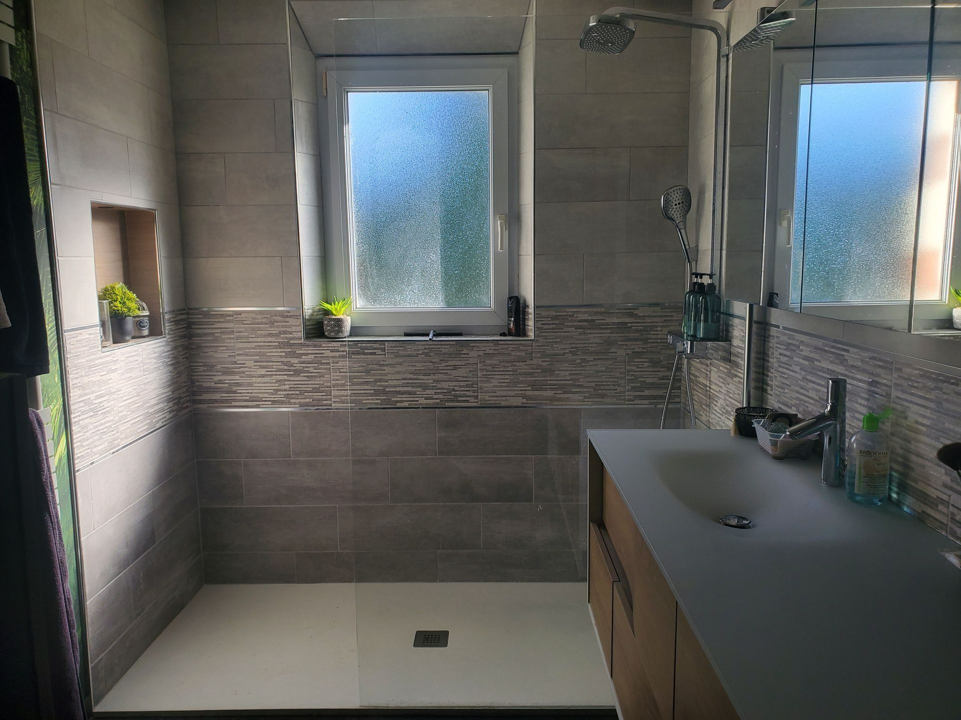 Salle de bains moderne avec douche à l'italienne, fenêtres dépolies, carrelage gris et meuble-lavabo en bois.