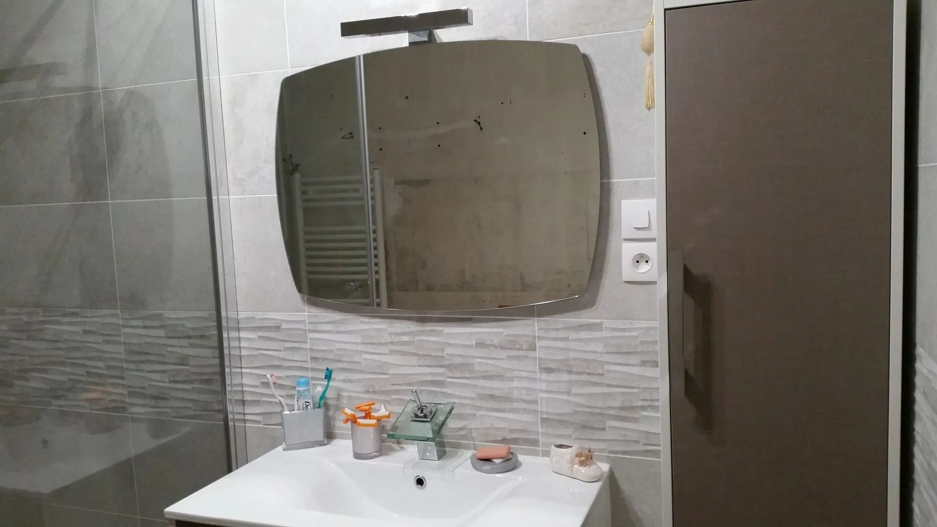 Meuble-lavabo avec lavabo, miroir et cabine de douche en verre à côté d'une porte marron.