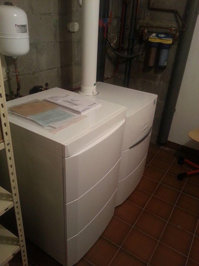 Des armoires de rangement blanches dans un sous-sol, avec des papiers dessus et des tuyaux de plomberie à proximité.