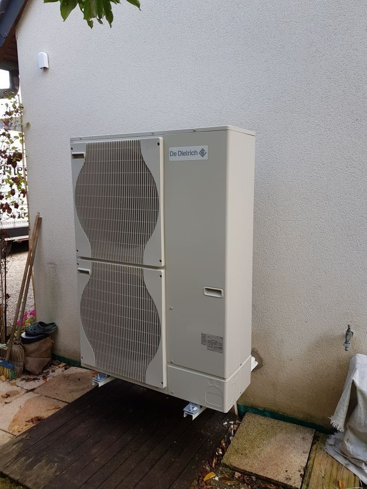 Unité de climatisation extérieure installée à côté d'un mur de la maison, avec deux grandes grilles de ventilation circulaires.