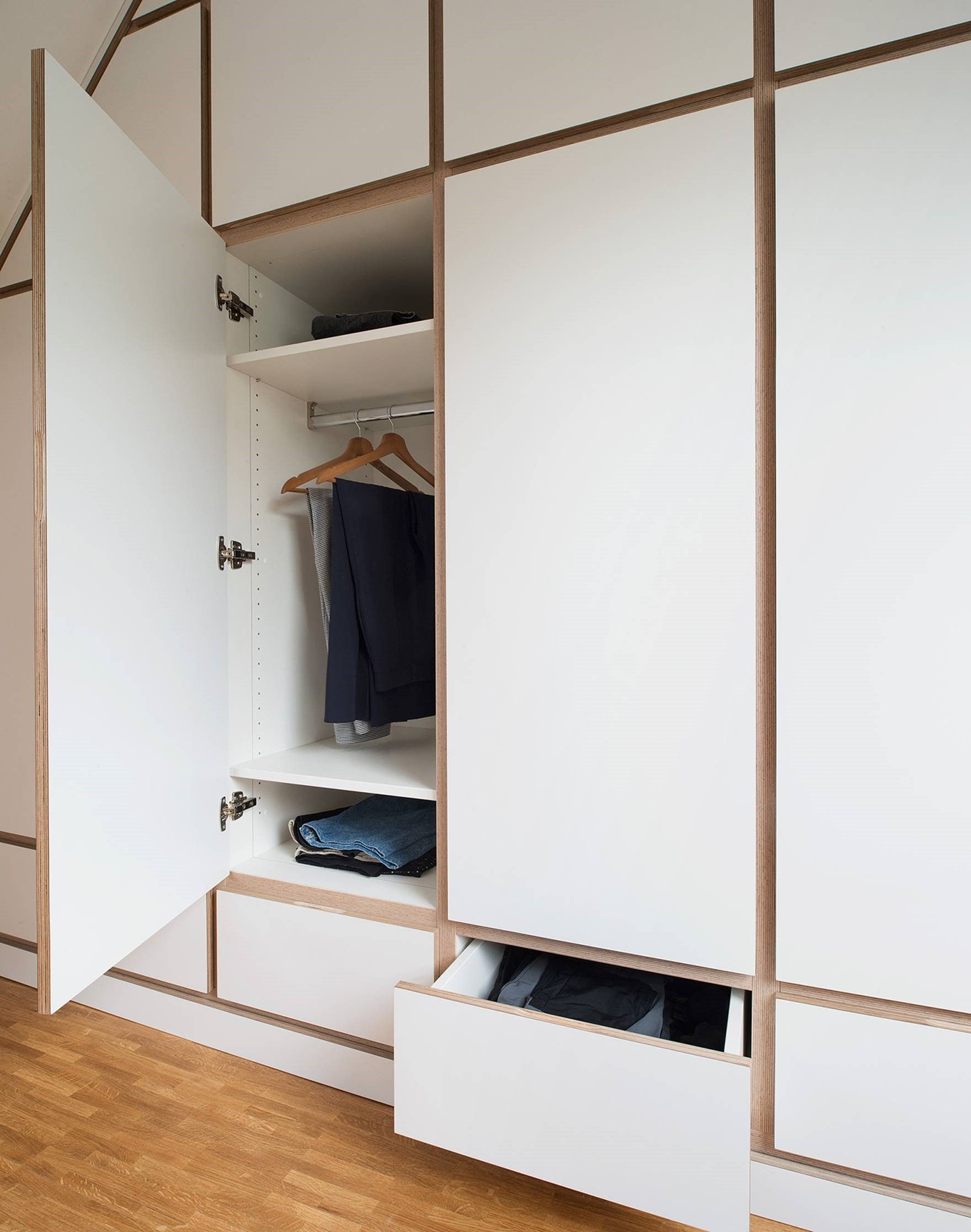 Offener Kleiderschrank mit weißen Schränken, durch die man hängende Kleidung und gefaltete Wäschestücke sieht.
