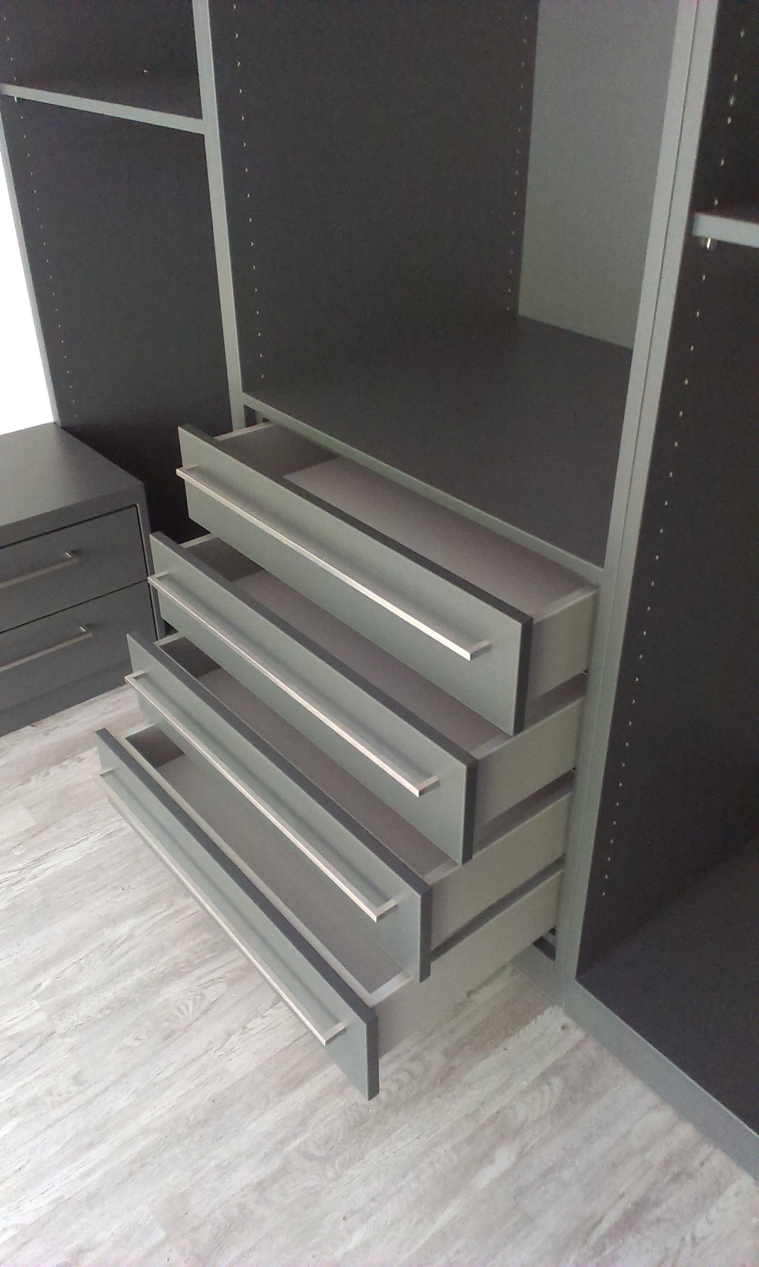Offene Schubladen in einem dunkelgrauen Kleiderschrank mit hellem Holzboden und weißen Griffen.