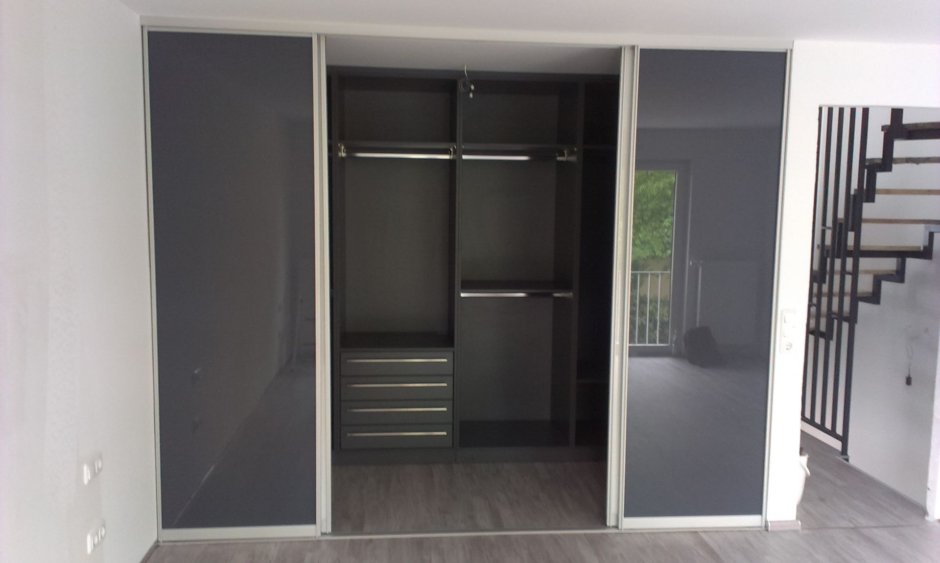 Ein leerer grauer Schrank mit Schiebetüren in einem modernen Zimmer, neben einer Treppe.