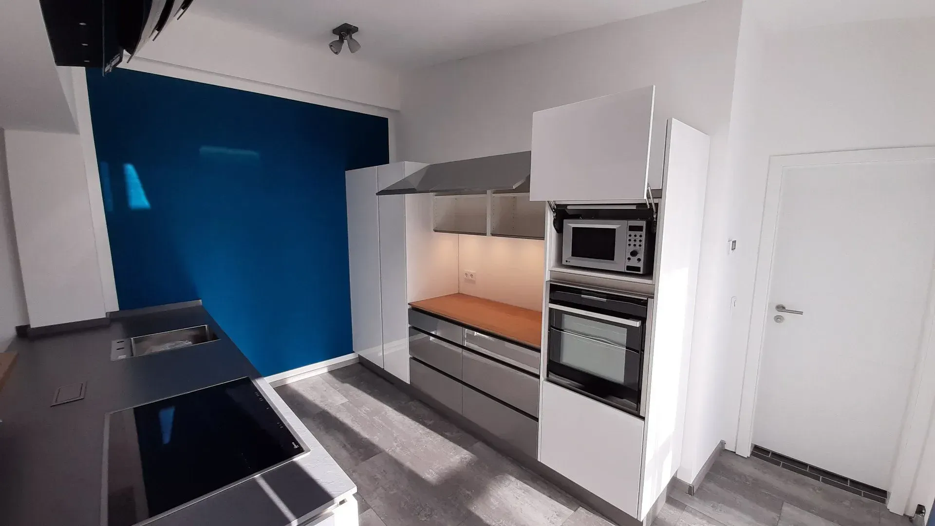 Moderne Küche mit blauer Akzentwand, weißen Schränken, dunklen Arbeitsplatten und Einbaubackofen