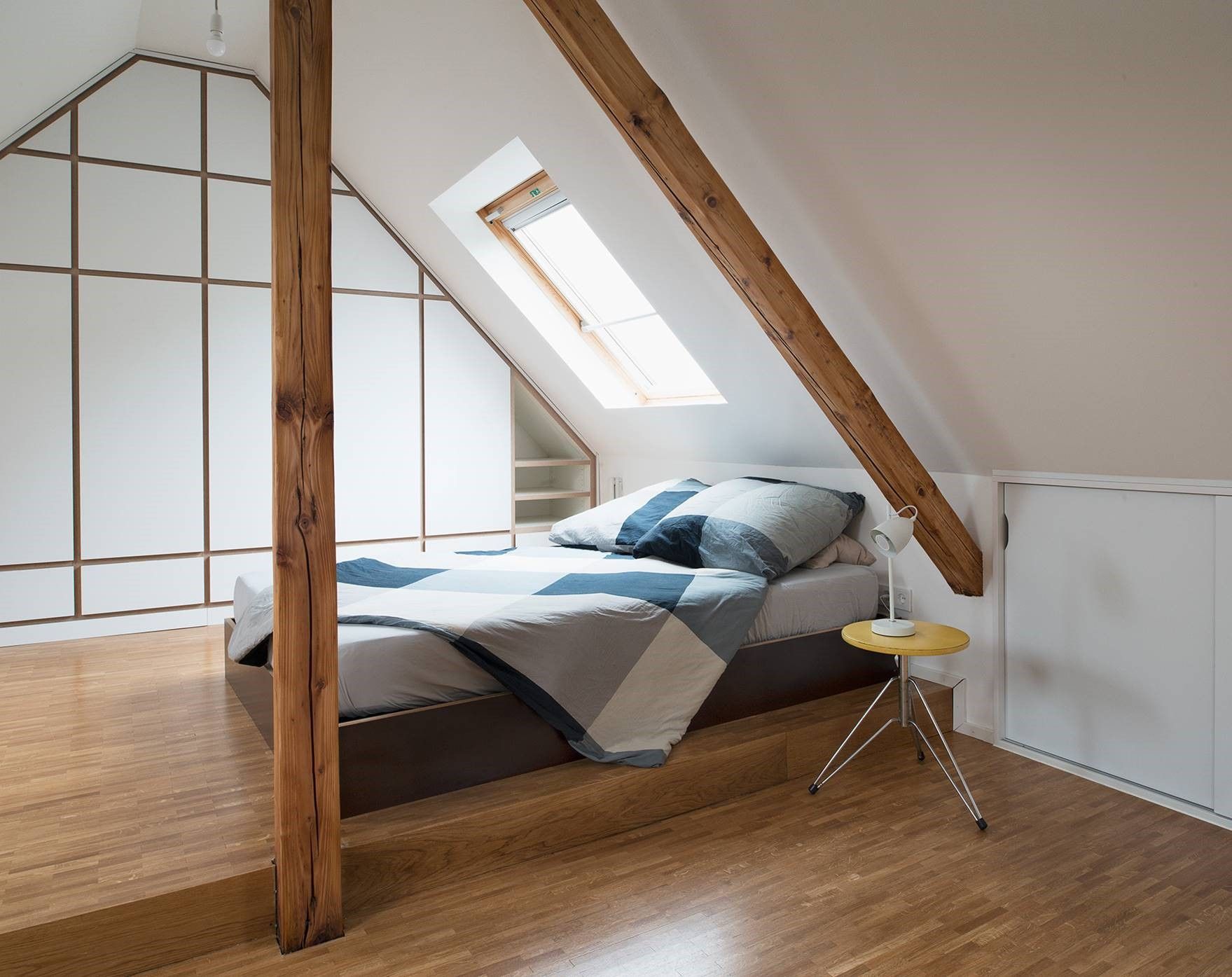 Loft-Schlafzimmer mit Dachschräge, Holzbalken, Bett, Dachfenster und Holzboden