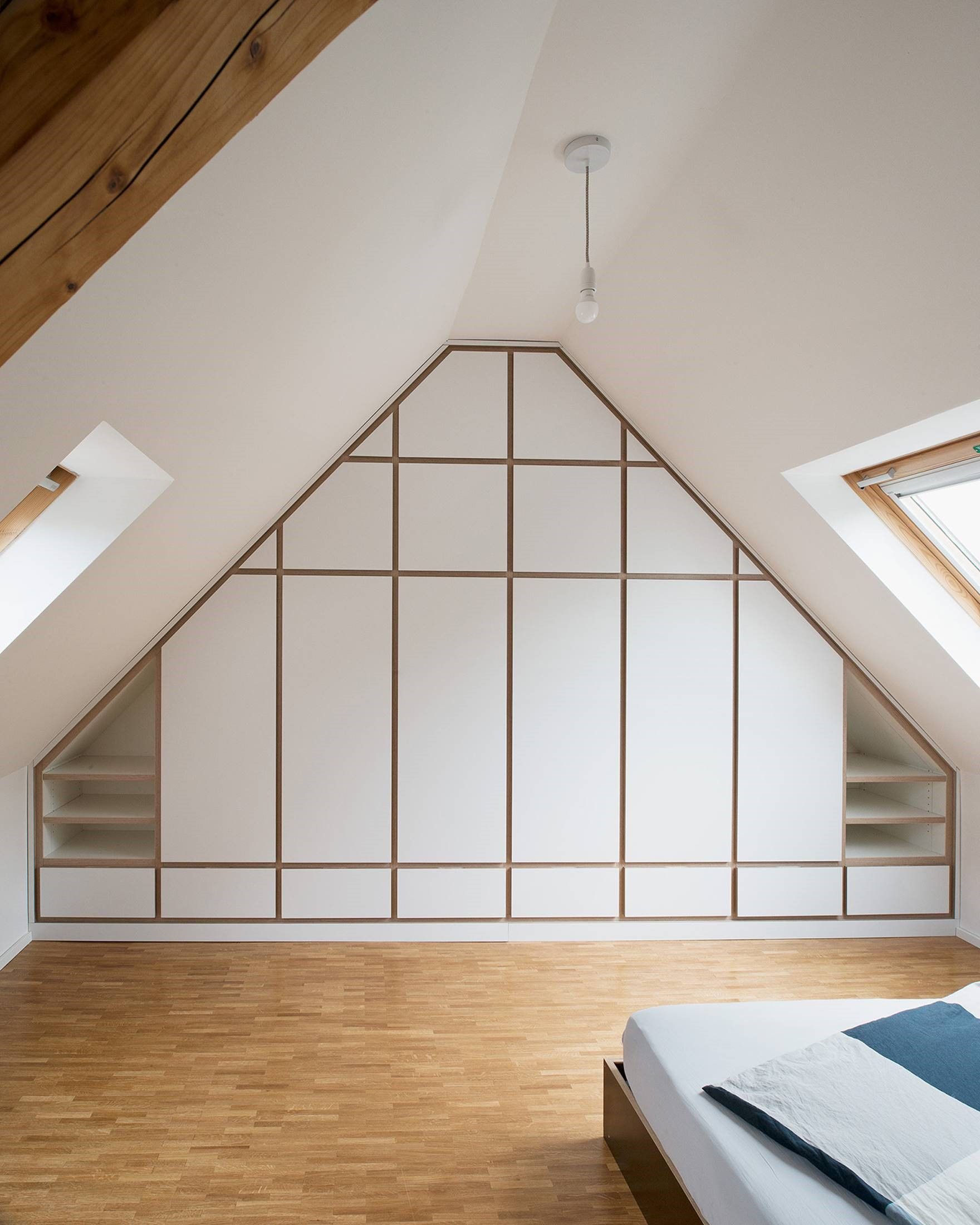 Dachgeschosszimmer mit weißen Dachschrägen, Einbauregalen und Holzboden mit einem Bett in der Ecke