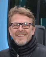 Ein lächelnder Mann mit Brille und dunkler Jacke 