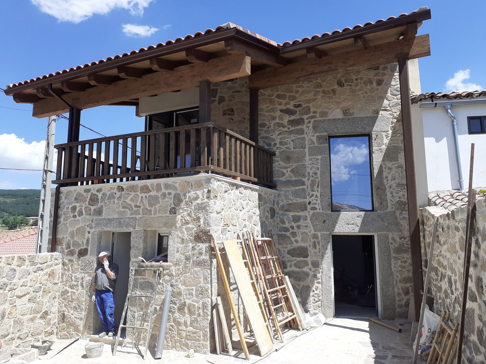 Casa de piedra en construcción con balcón, hombre en la puerta.