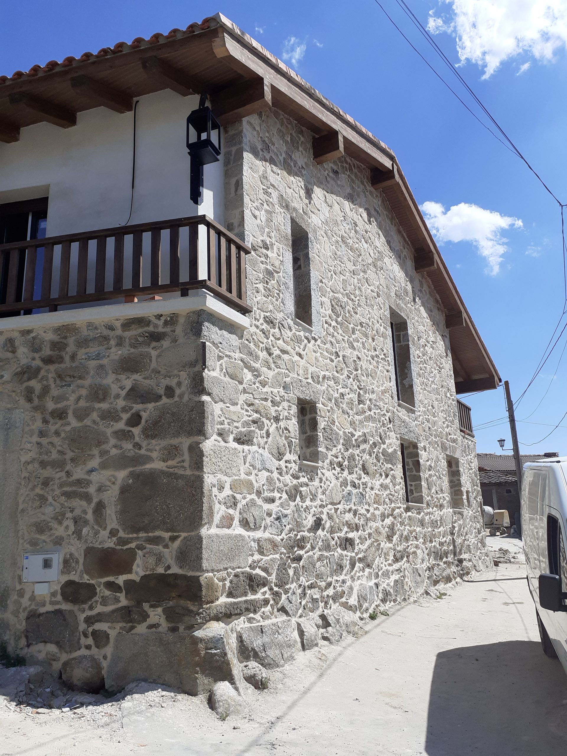 Edificio de piedra con balcón y alero de madera bajo un cielo azul brillante.