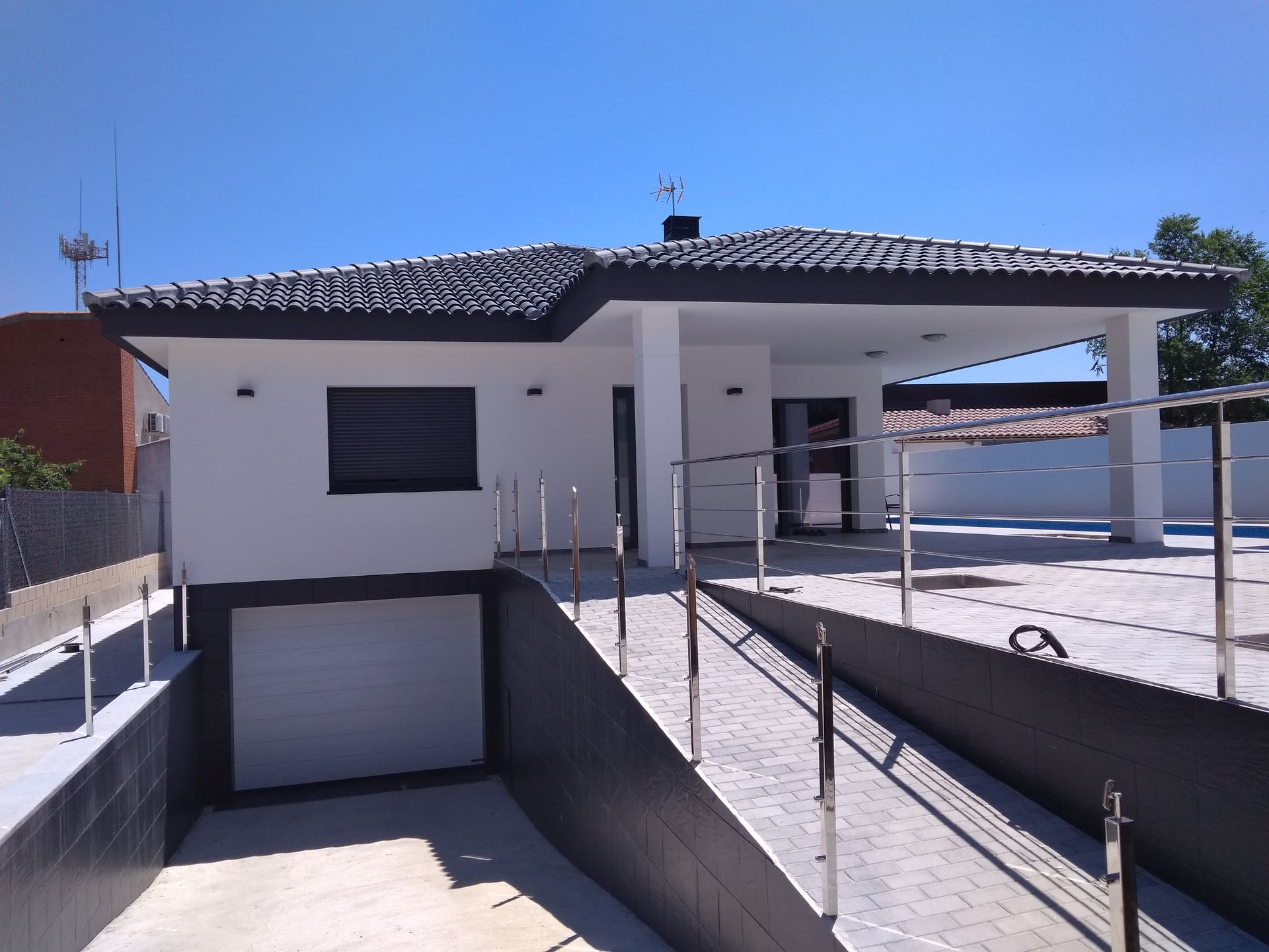 Casa blanca con techo oscuro y entrada al garaje, con rampa con barandillas.