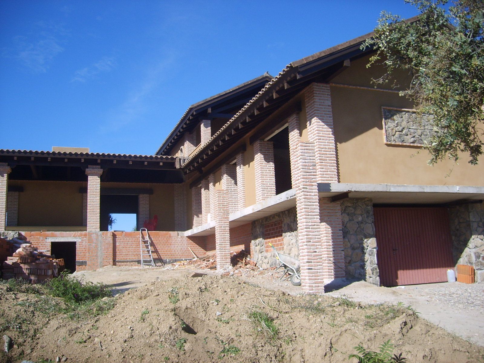Edificio en construcción con columnas de ladrillo a la vista y fachada marrón, contra un cielo azul claro.