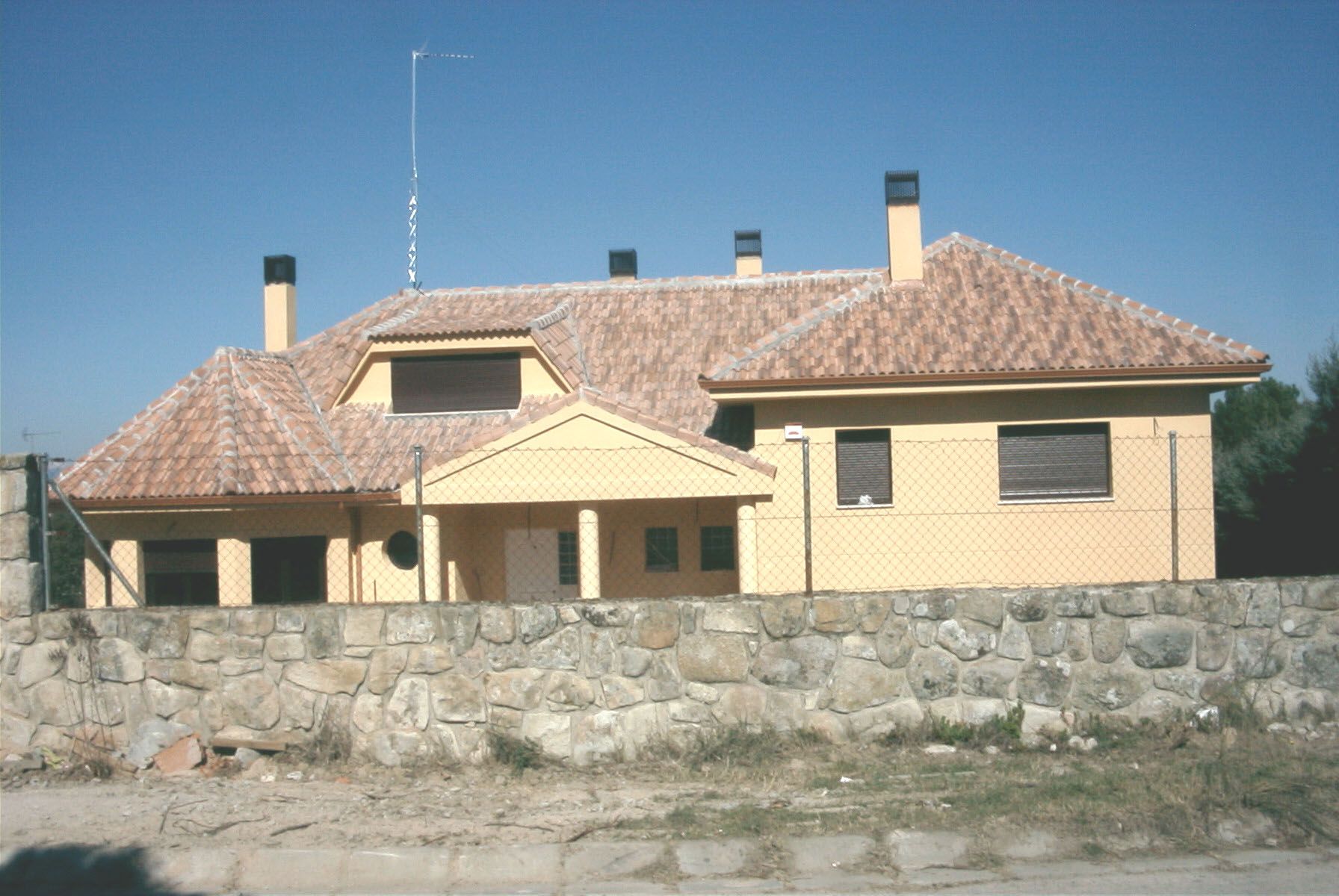 Casa color canela con techo de terracota y pared de piedra en un día soleado.