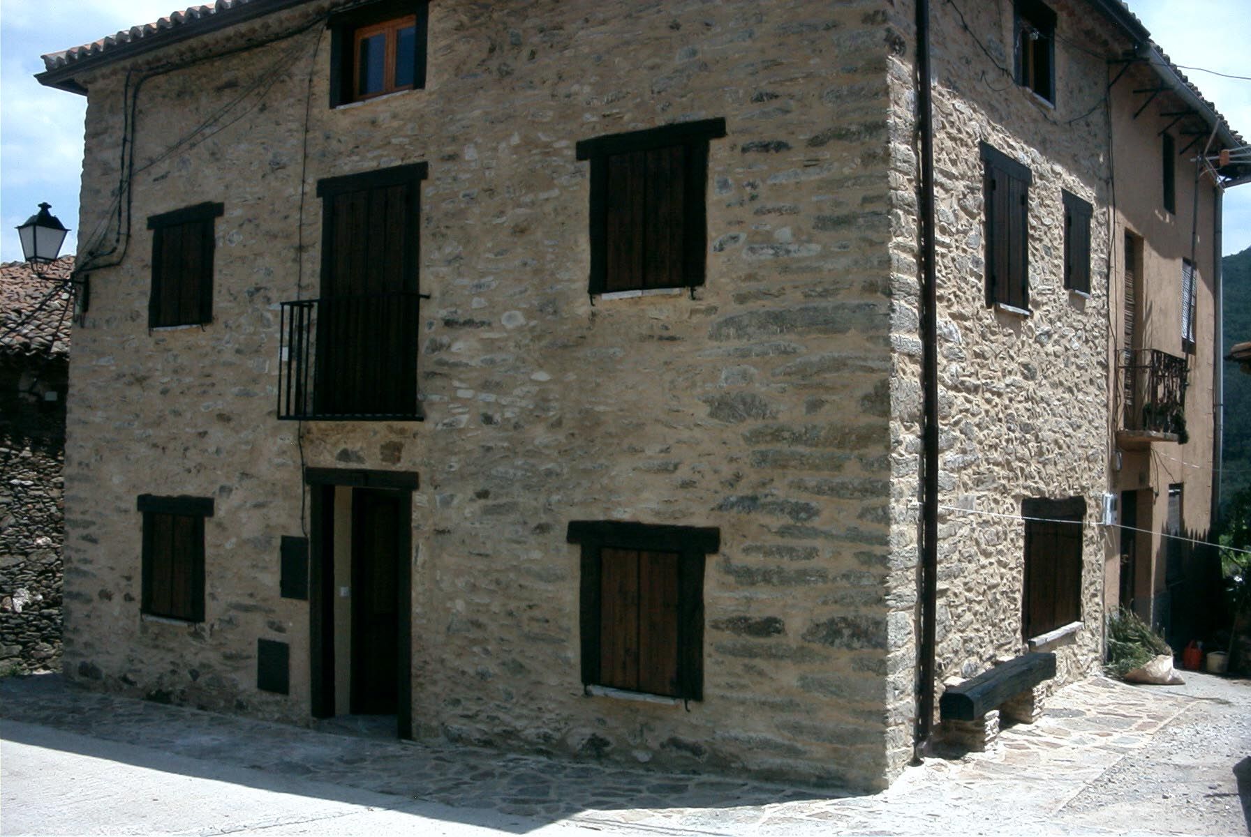 Edificio de piedra con contraventanas y puerta oscuras, pequeño balcón.