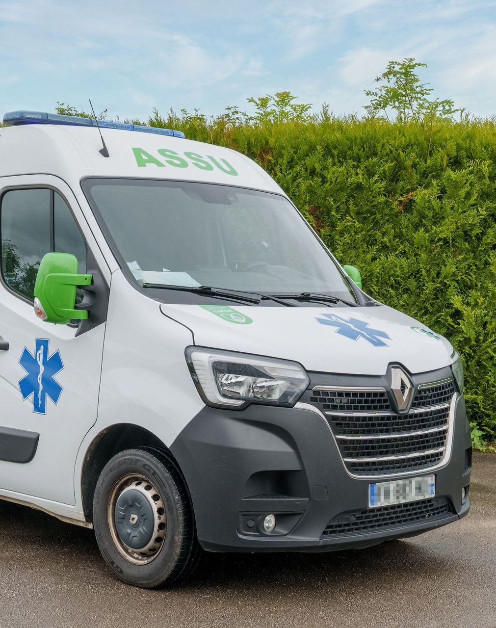 Une ambulance blanche devant une haie