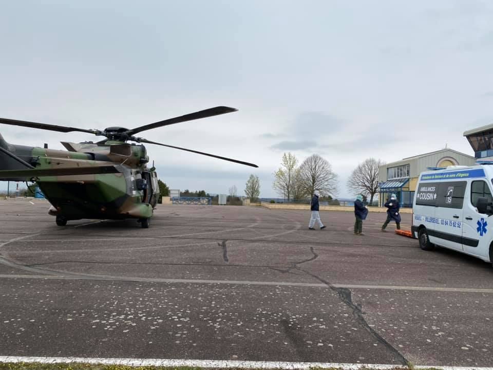 Un hélicoptère militaire à gauche d'une piste et une ambulance sur la droite