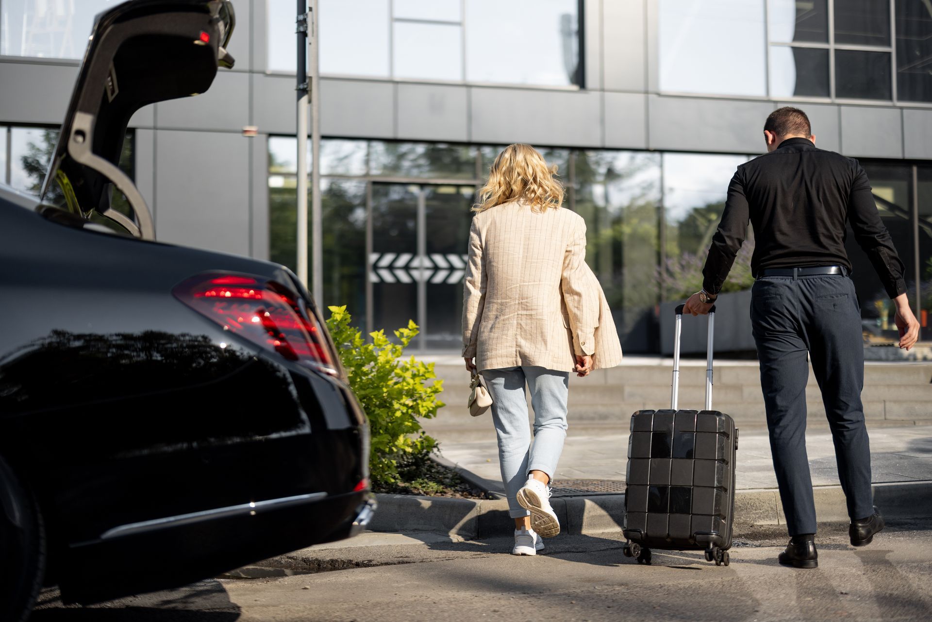 Une femme et un homme en costume avec une valise  se dirigent vers un hôtel