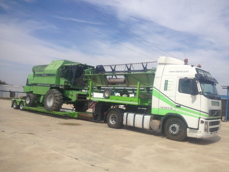 Un camión verde y blanco transporta una cosechadora en un remolque.