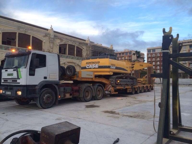 Un camión blanco transporta una excavadora amarilla en un remolque.