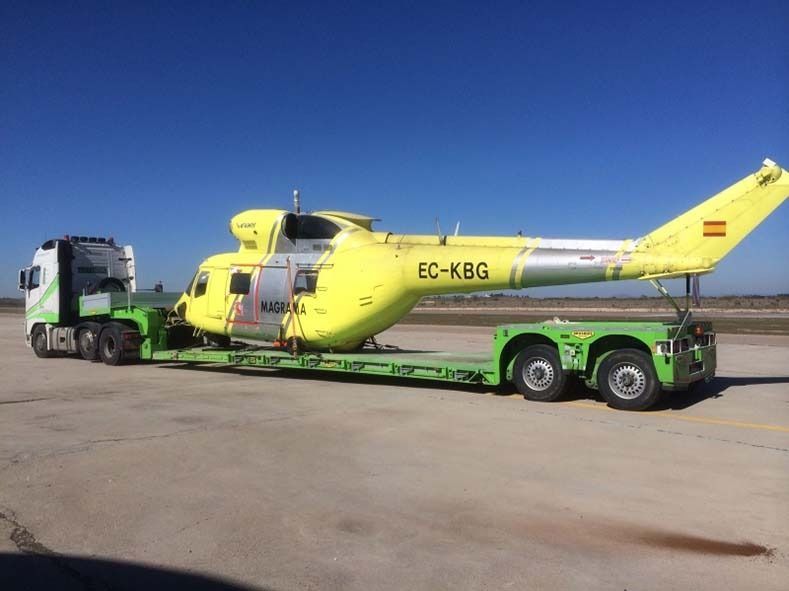 Un helicóptero amarillo está siendo transportado en un remolque verde.