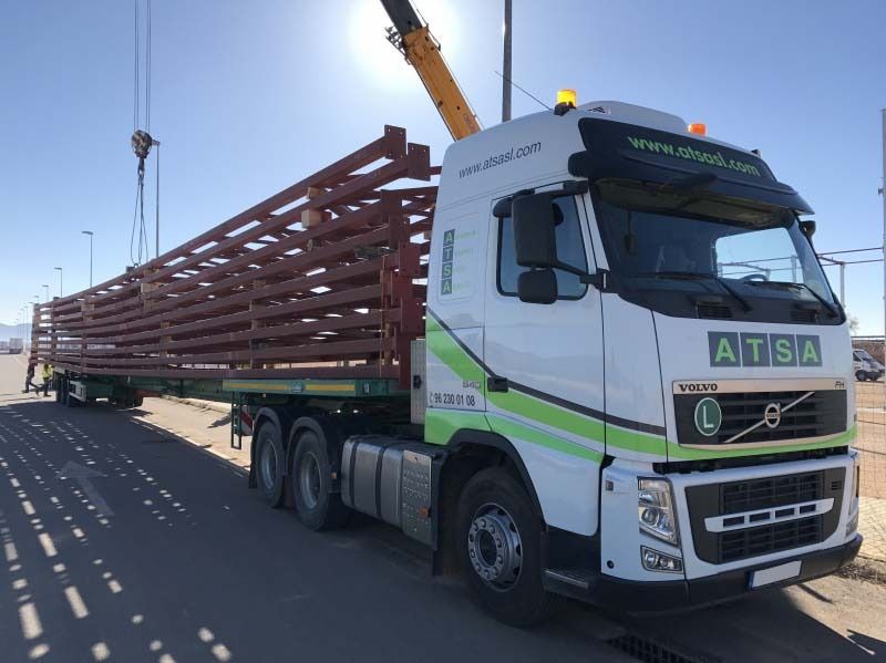Un camión blanco con una grúa en la parte trasera transporta una carga muy larga.