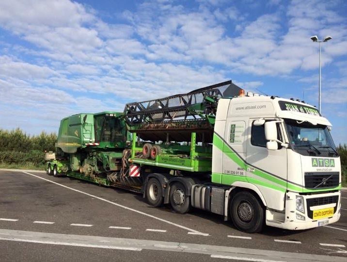 Un camión verde y blanco transporta una cosechadora.