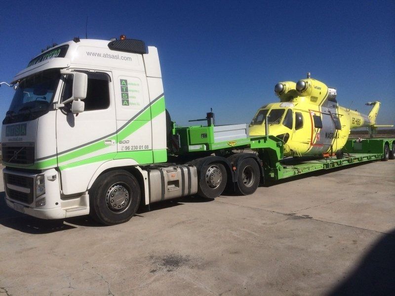 Un helicóptero amarillo está siendo transportado por un camión semirremolque blanco y verde.