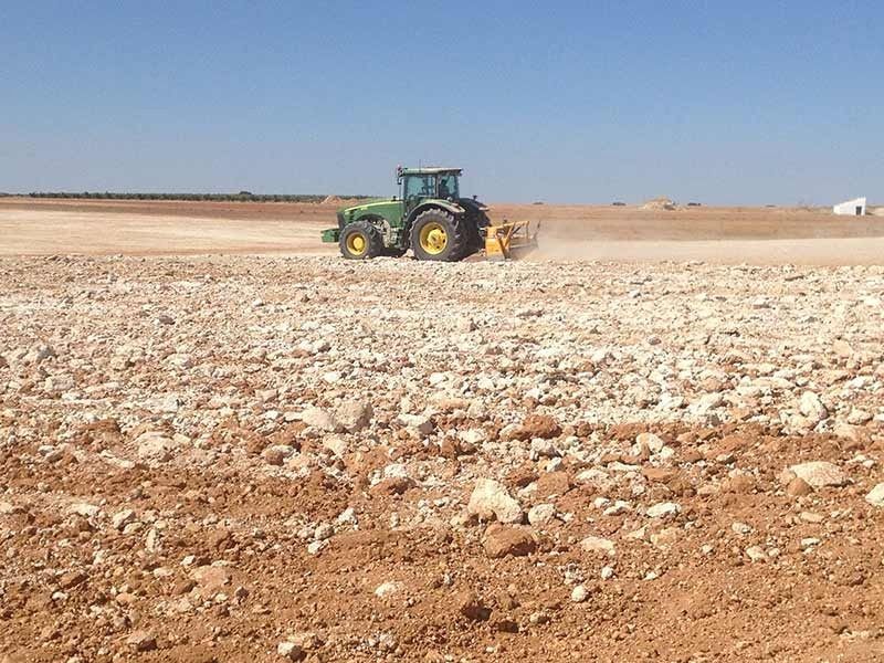 Un tractor verde está arando un campo rocoso