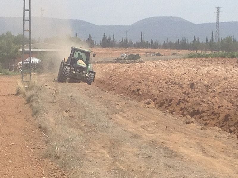 Un tractor está arando un camino de tierra con montañas al fondo.