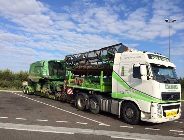 Un camión verde y blanco transporta una cosechadora.