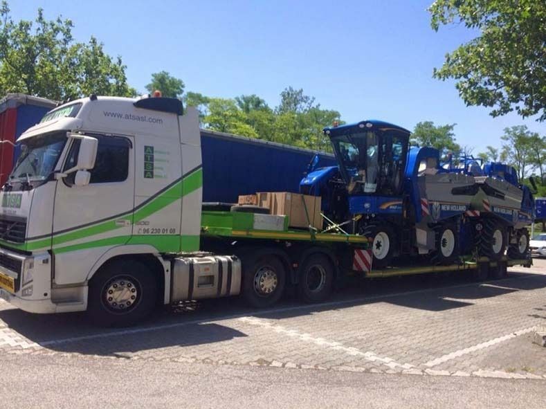 Un camión semirremolque blanco y verde con tractores en la parte trasera está estacionado en un estacionamiento.