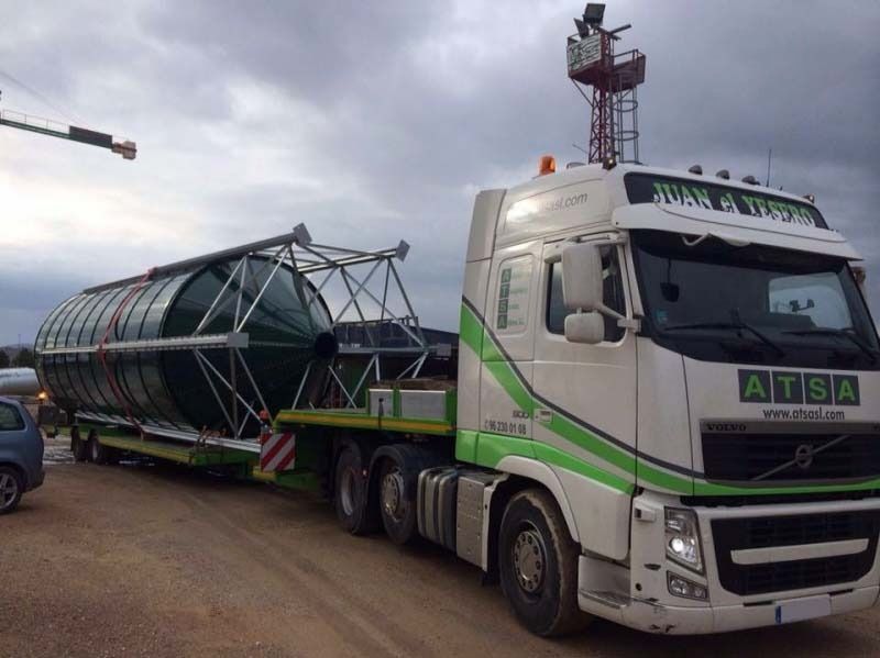 Un camión semirremolque blanco y verde transporta un objeto grande.