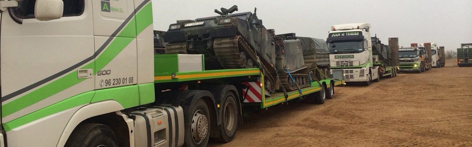 Una fila de camiones están estacionados en un campo de tierra.