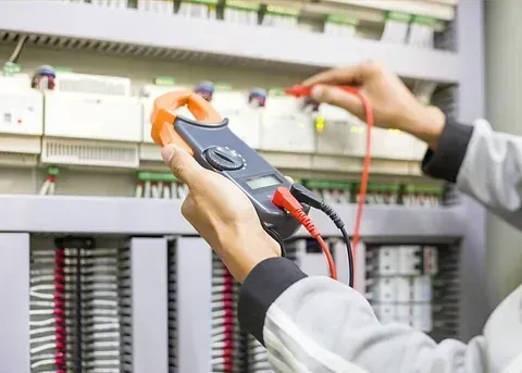 Una persona usa una pinza amperimétrica para probar componentes eléctricos dentro de un panel de control. Las sondas roja y negra están conectadas.