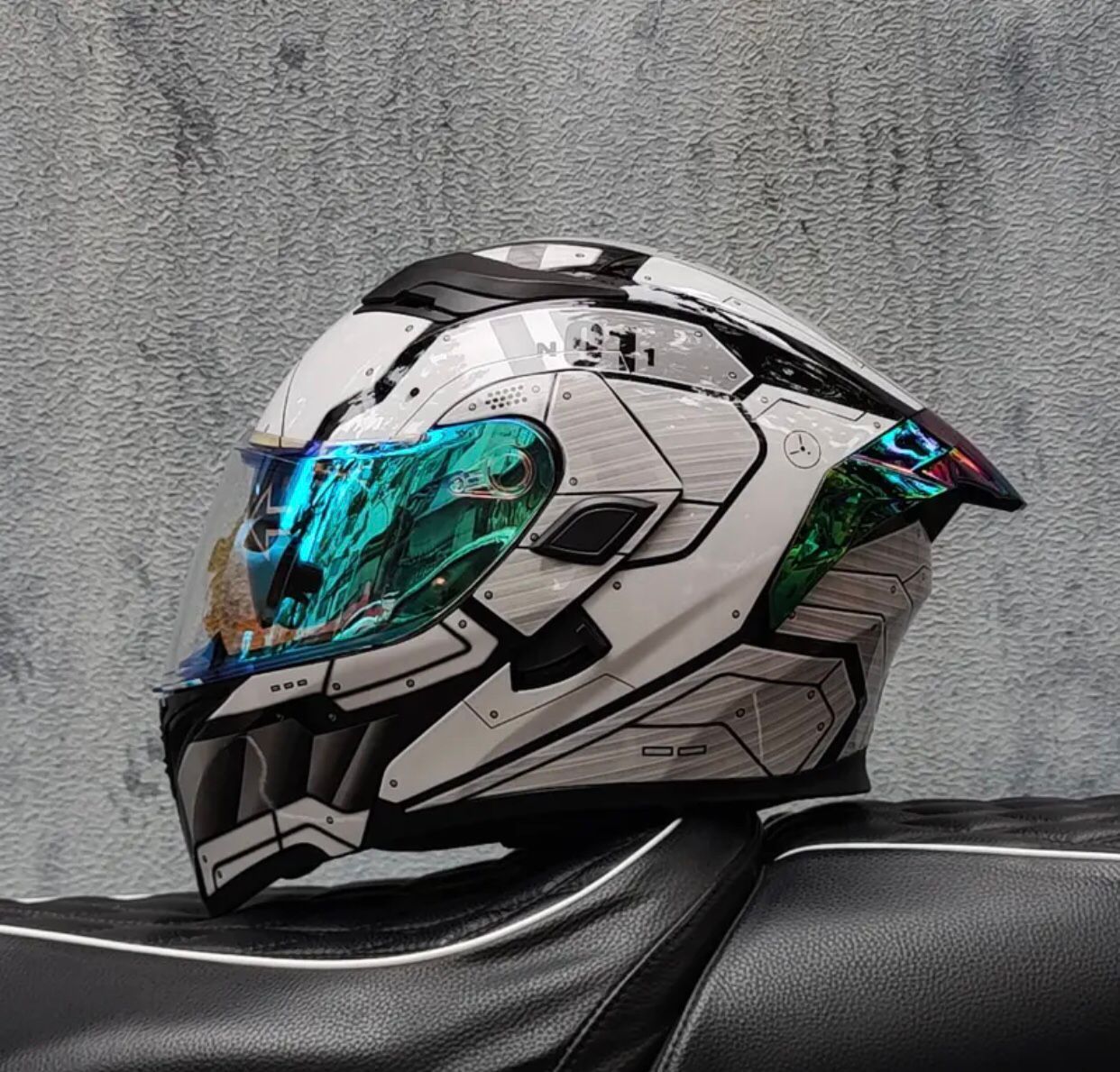 Casco de motocicleta blanco y gris con visera verde azulado, apoyado sobre un asiento negro.