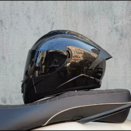 Casco de motocicleta negro brillante con patrón de fibra de carbono sobre un asiento negro.