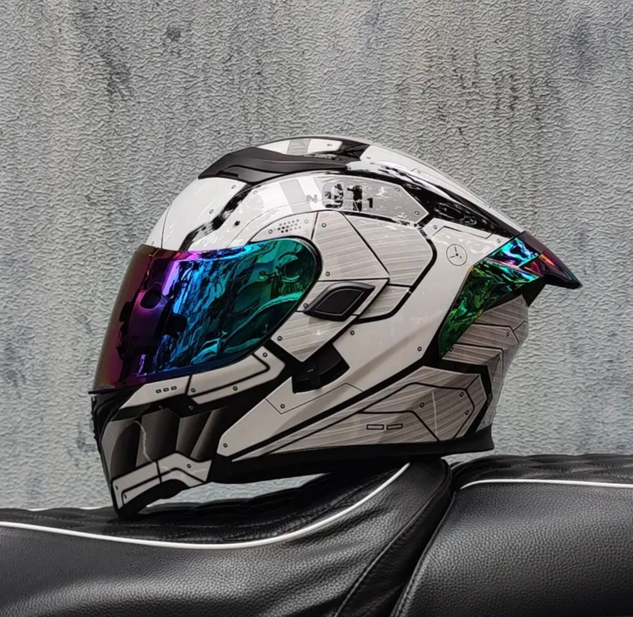 Casco de motocicleta blanco y negro con visera multicolor, apoyado sobre un asiento negro.