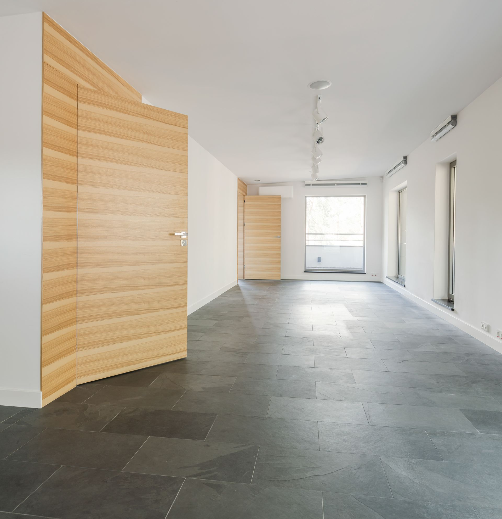 Pièce vide avec sol carrelé gris foncé, murs blancs et portes en bois.