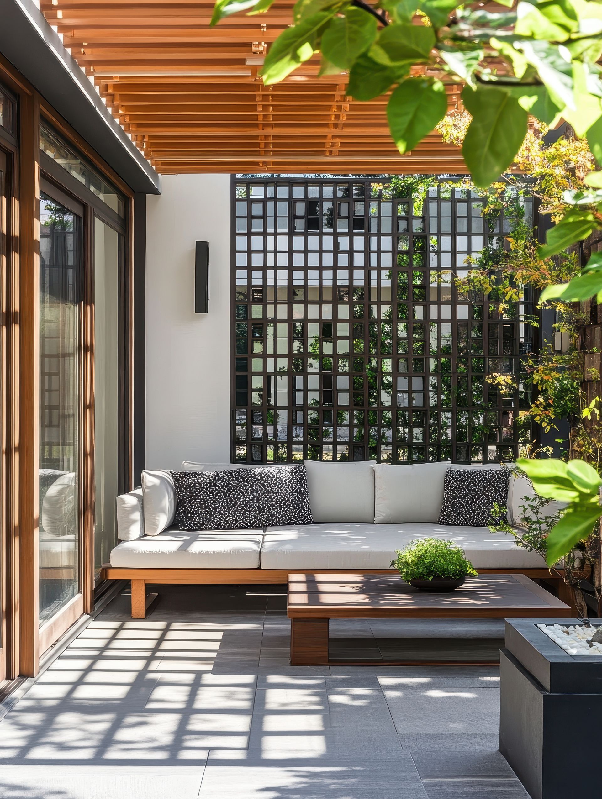 Terrasse extérieure avec mobilier en bois, treillis et coussins, où la lumière du soleil projette des ombres sur le sol.