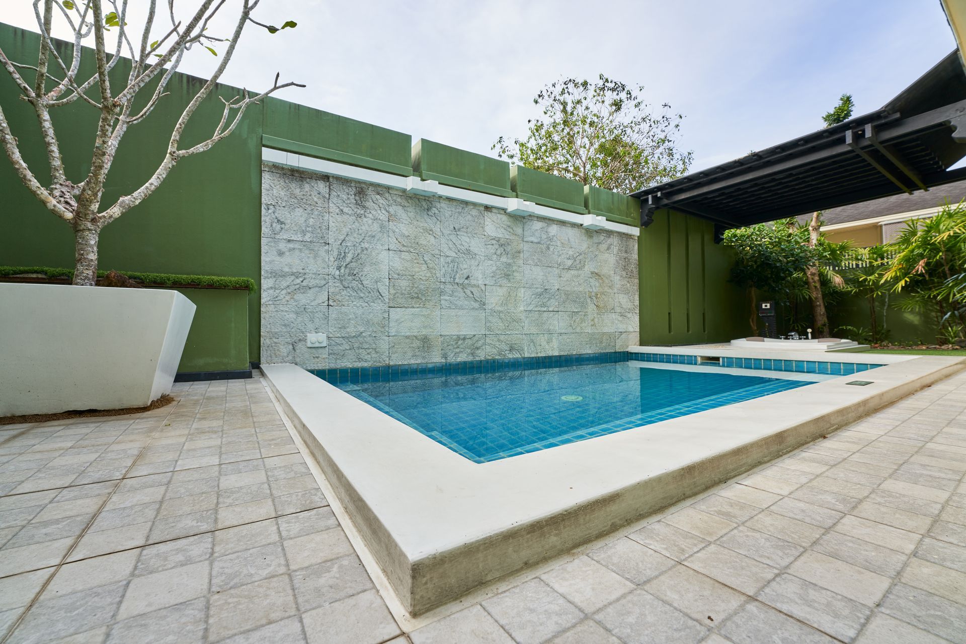 Petite piscine extérieure rectangulaire avec cascade et entourée d'une terrasse.