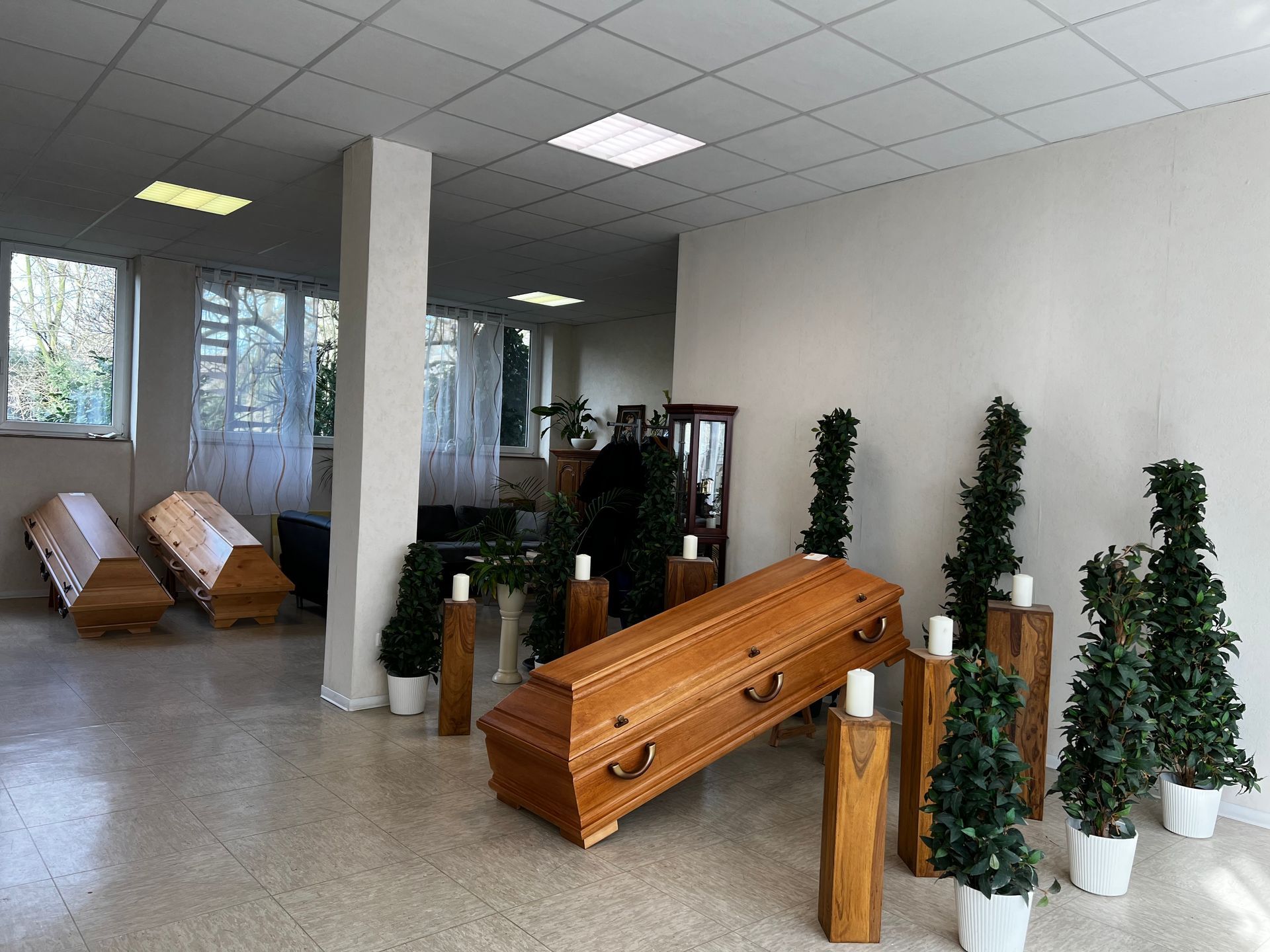 Ein Holzsarg steht auf einem Tisch in einem Raum, umgeben von Topfpflanzen und Kerzen. Foto von den Bestattungen Jeup