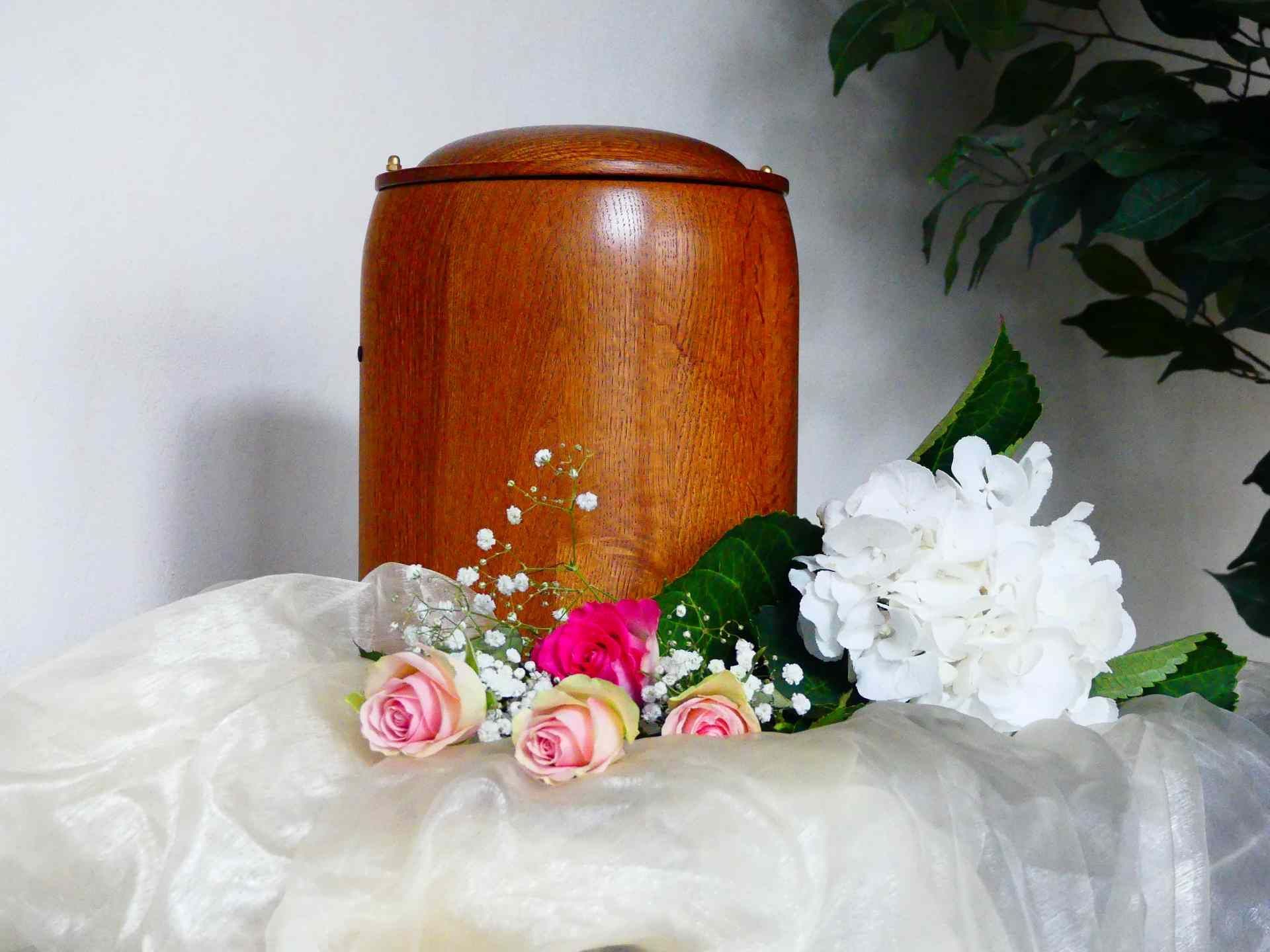 Eine hölzerne Urne ist von Blumen umgeben auf einem Tisch. Foto von den Bestattungen Jeup