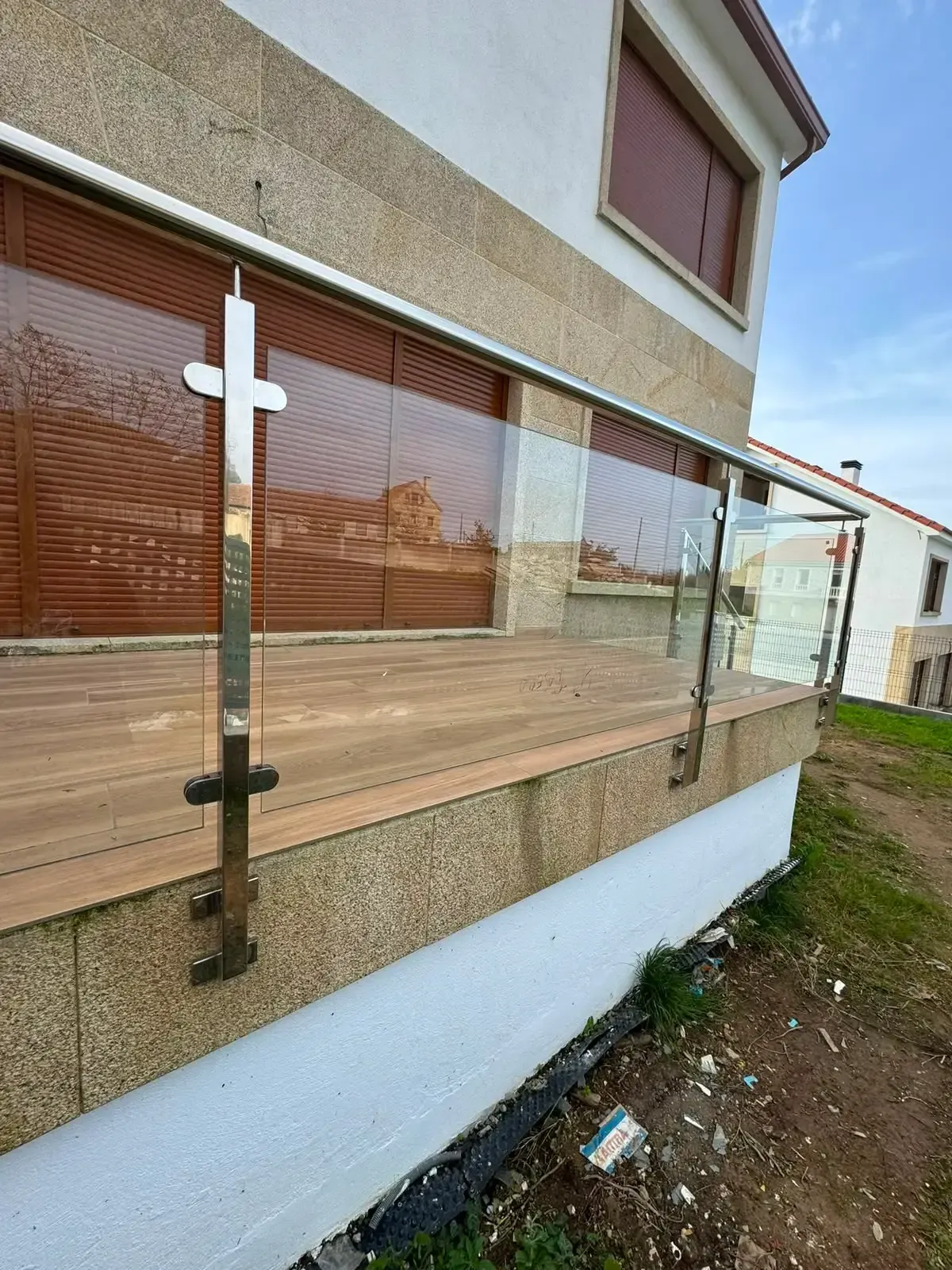 Barandilla de cristal en un balcón adosada a un edificio beige sobre un camino de tierra.