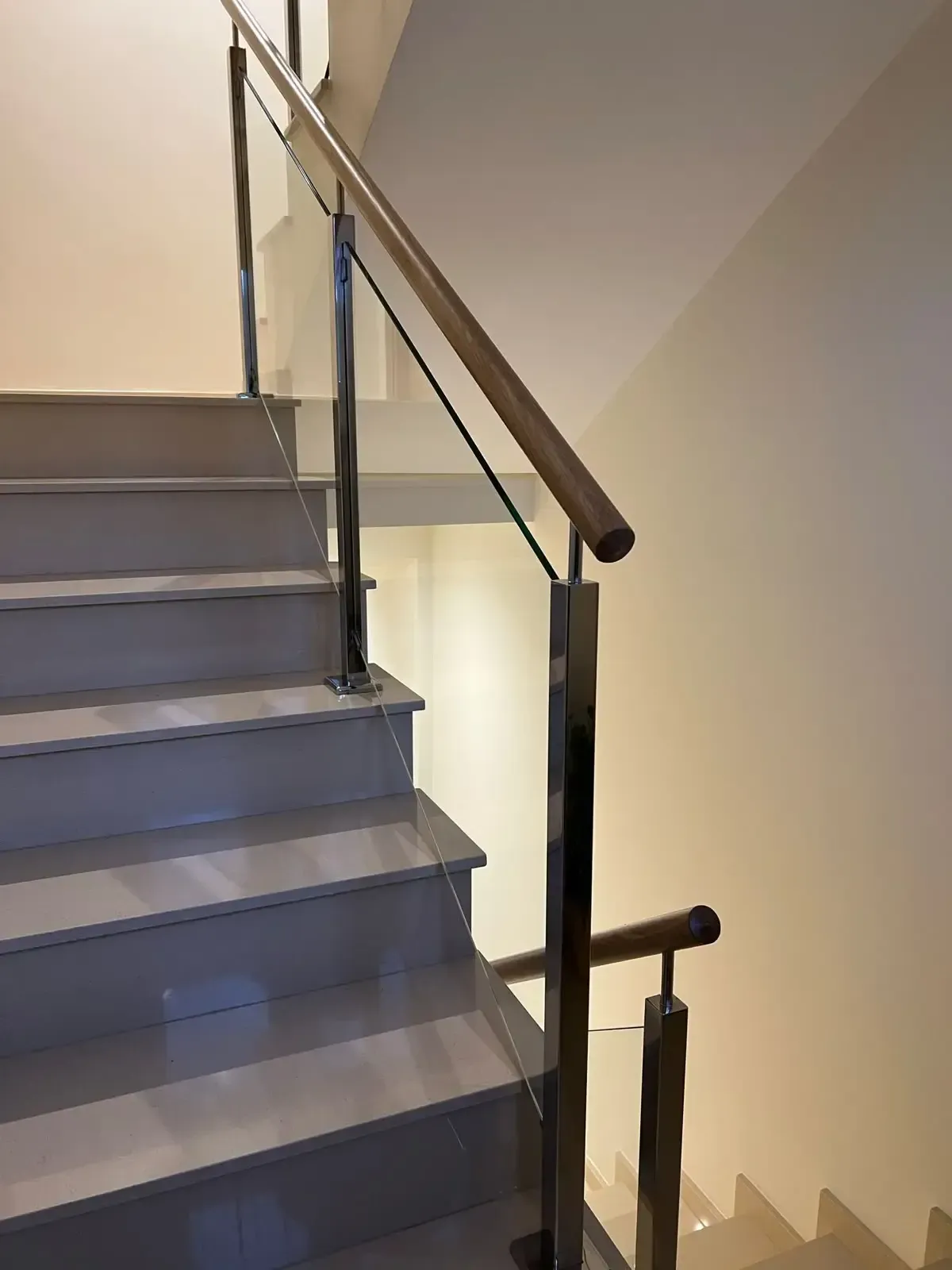 Escalera interior con escalones grises y pasamanos negro sobre una pared beige.