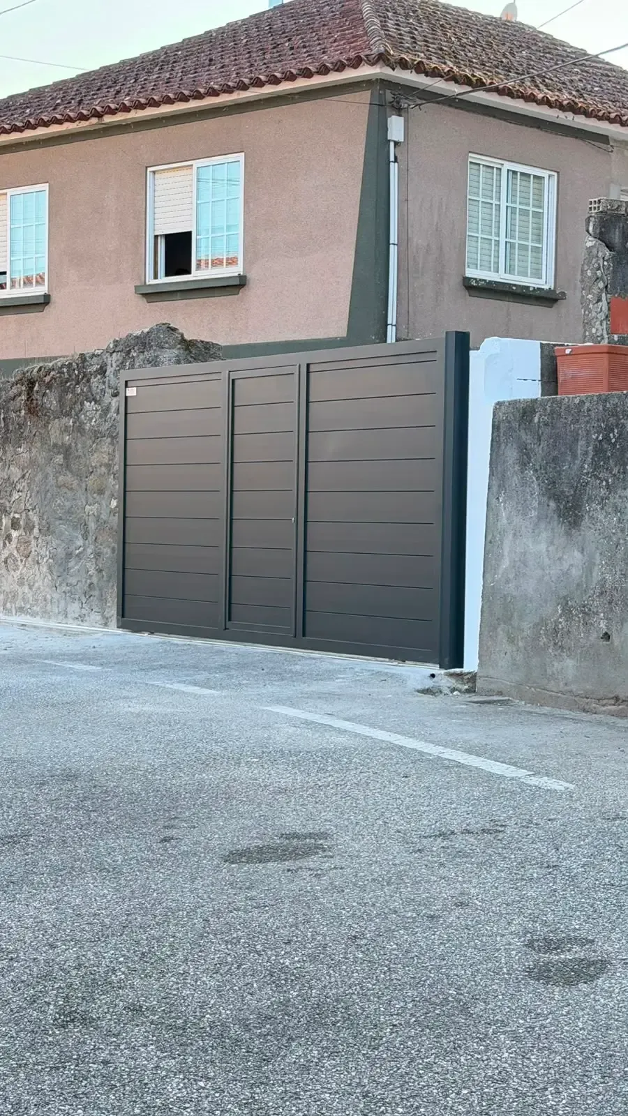 Casa residencial con portón gris y paredes exteriores de estuco rosa en una calle tranquila.