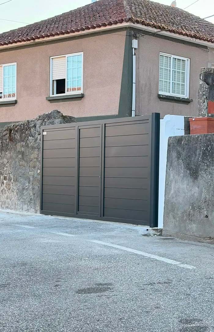 Casa marrón con ventanas con contraventanas detrás de una verja alta de color gris y un muro de piedra, en una esquina