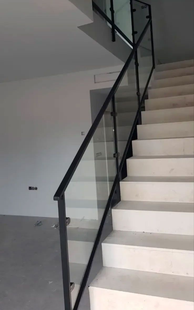 Escalera interior con peldaños blancos, barandilla negra y paredes grises en el pasillo de un edificio