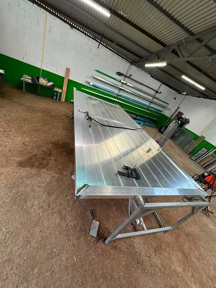Mesa de fabricación de metal en un taller, con una gran lámina brillante inclinada sobre un bastidor bajo luces fluorescentes.