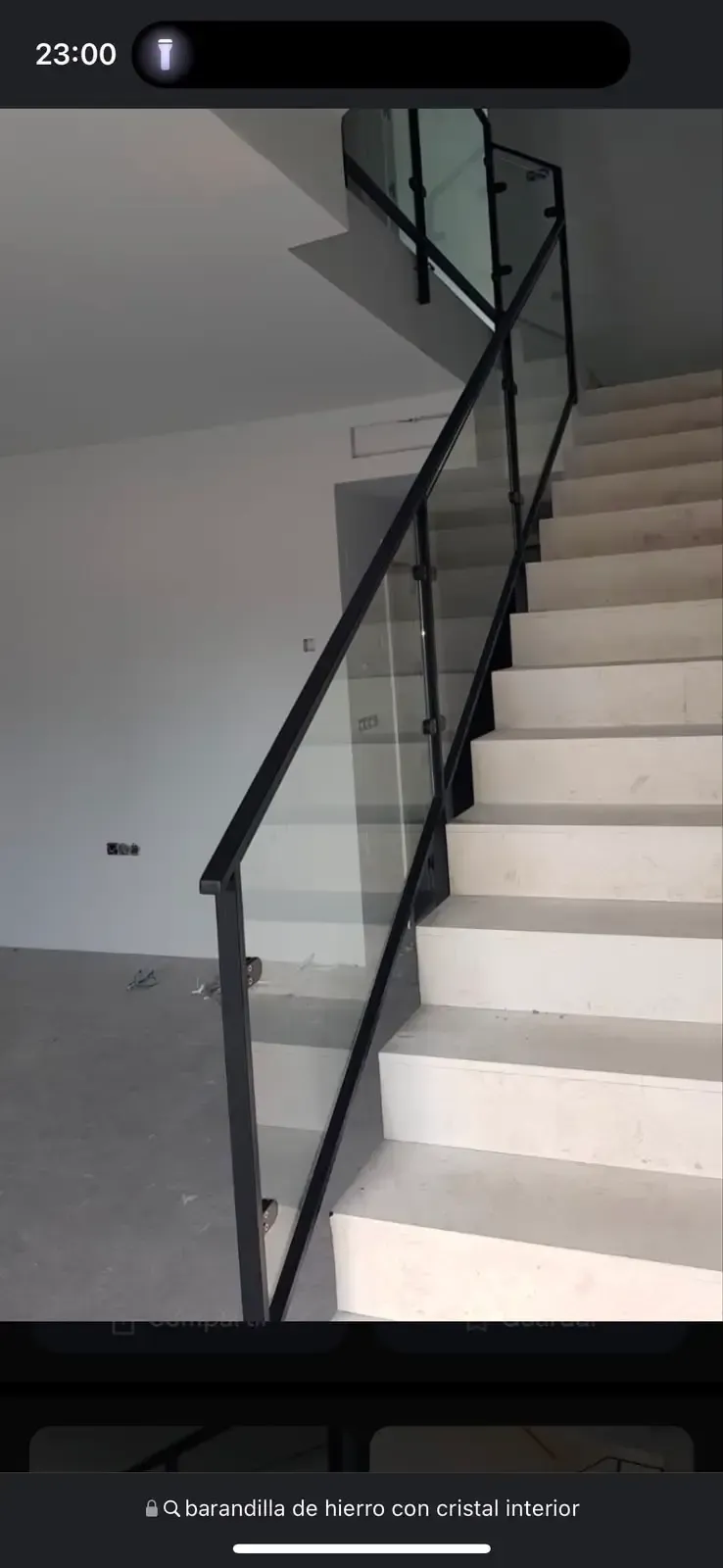 Escalera interior con escalones blancos, pasamanos negro y barandilla de cristal en un edificio moderno.