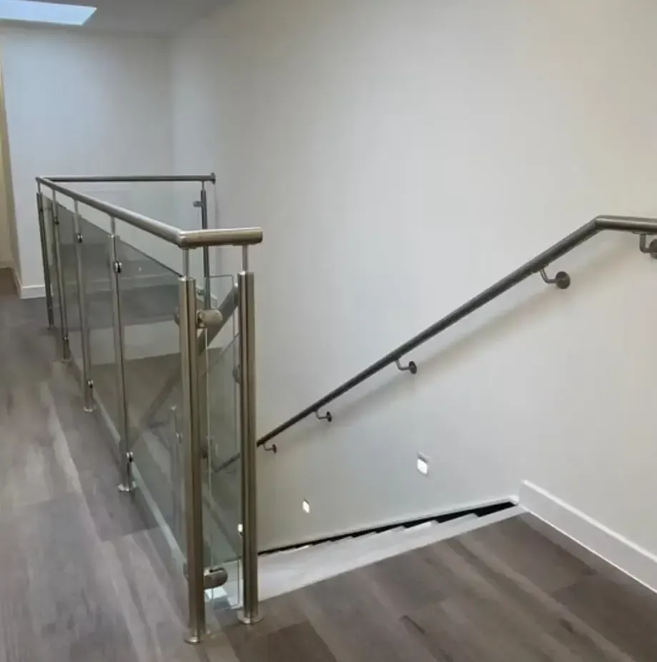 Escalera interior moderna con barandilla de cristal y una escalera descendente a la derecha.