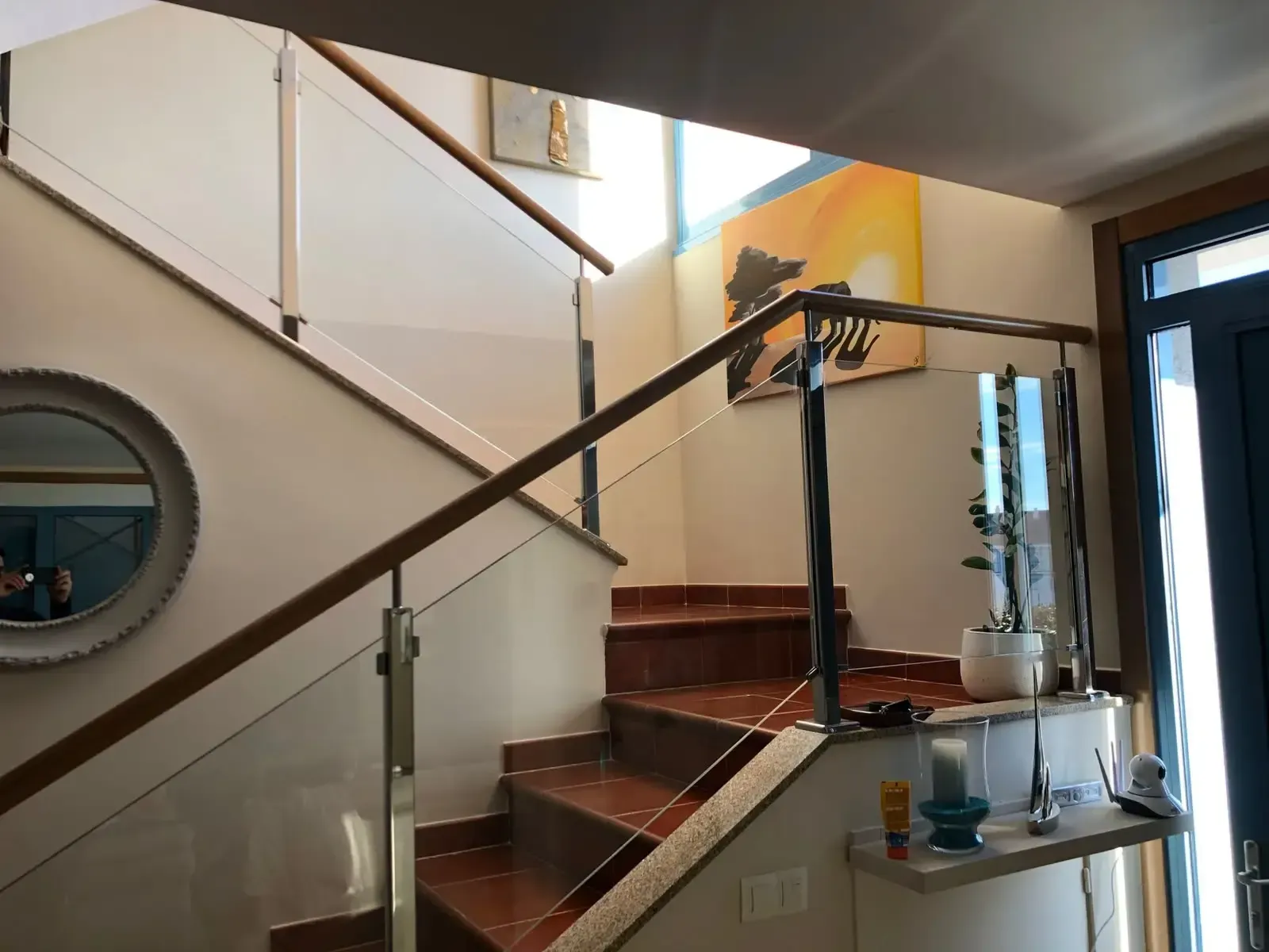 Escalera moderna con barandilla de cristal, escalones de madera y barra de mármol en un interior luminoso.